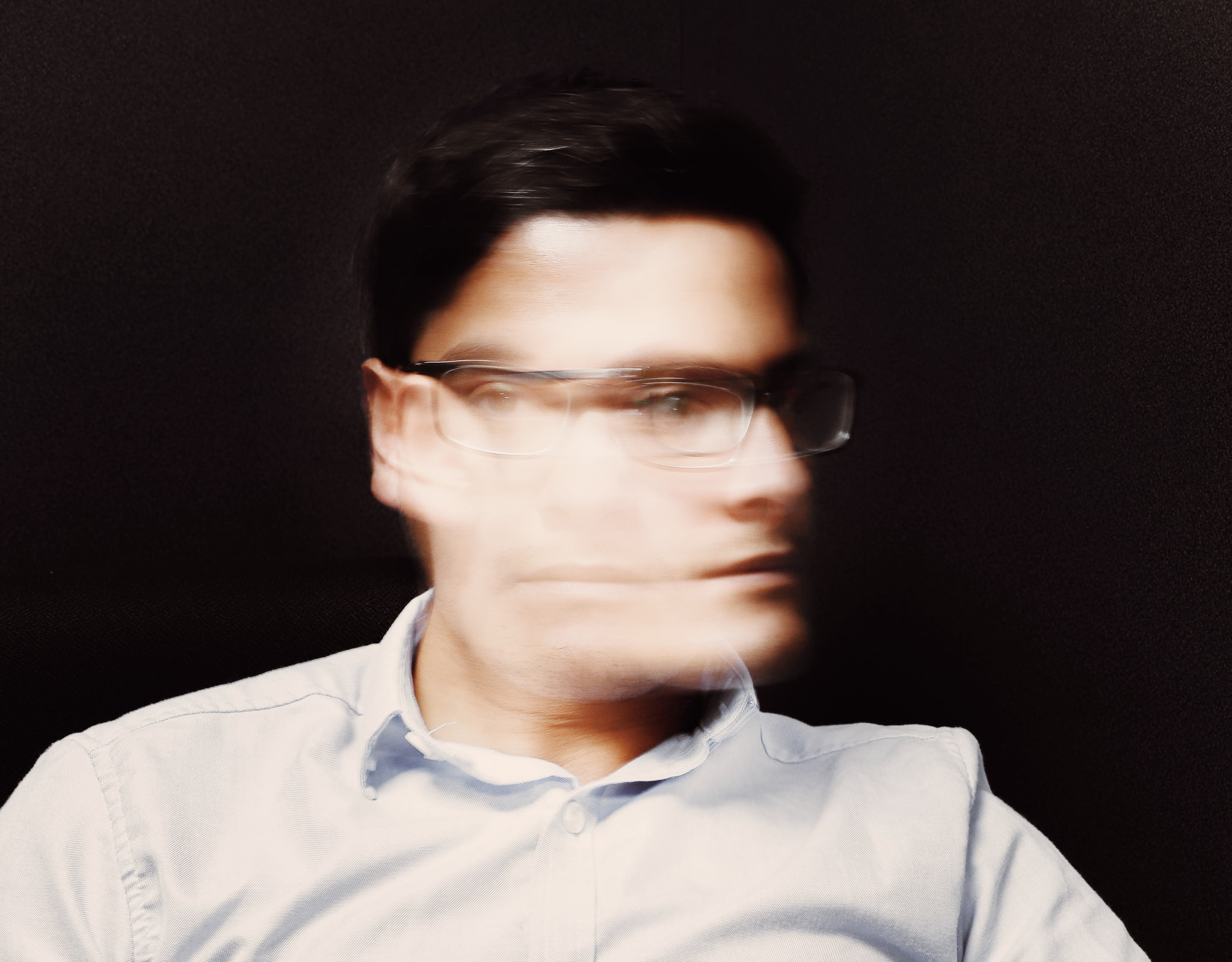 A blurry image of a man wearing glasses and shaking his head.