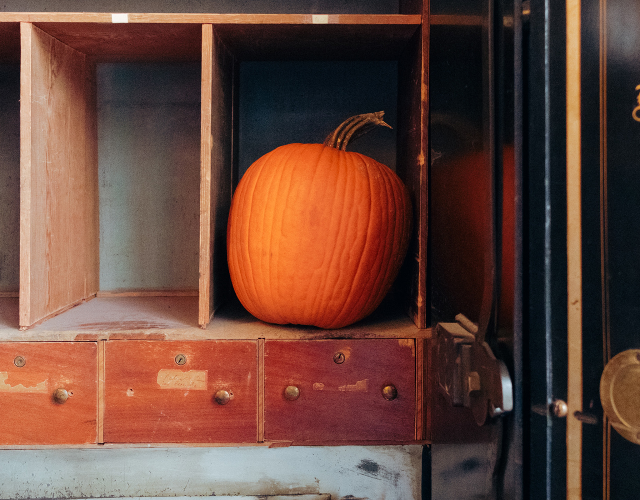 A pumpkin sits on an old shelf.